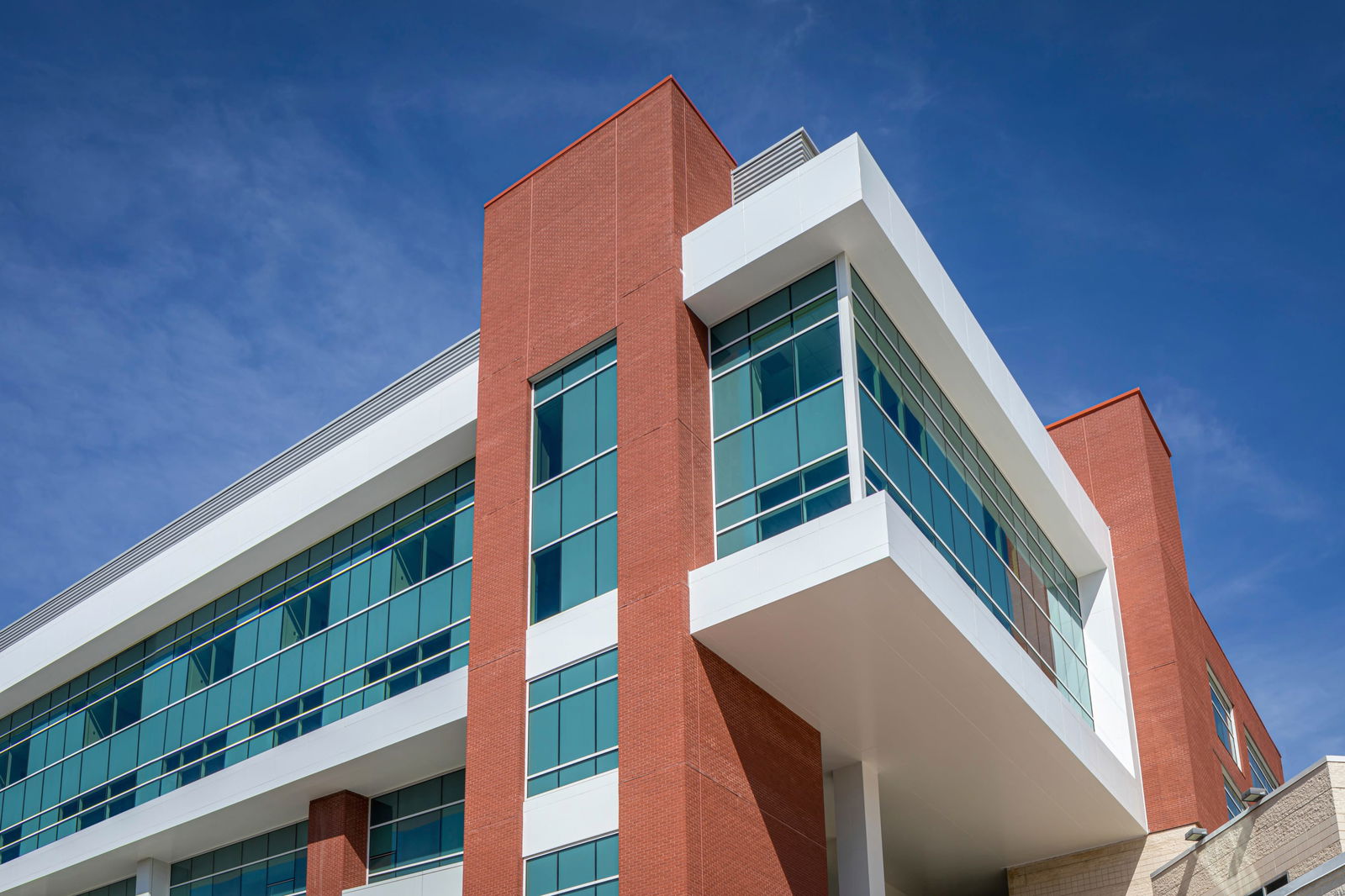 Close up view looking up at the WakeMed Cary Hospital, a modern multi-story medical facility building with red brick and white exterior with large glass windows. The closeness of this image allows one to appreciate the architectural design elements.