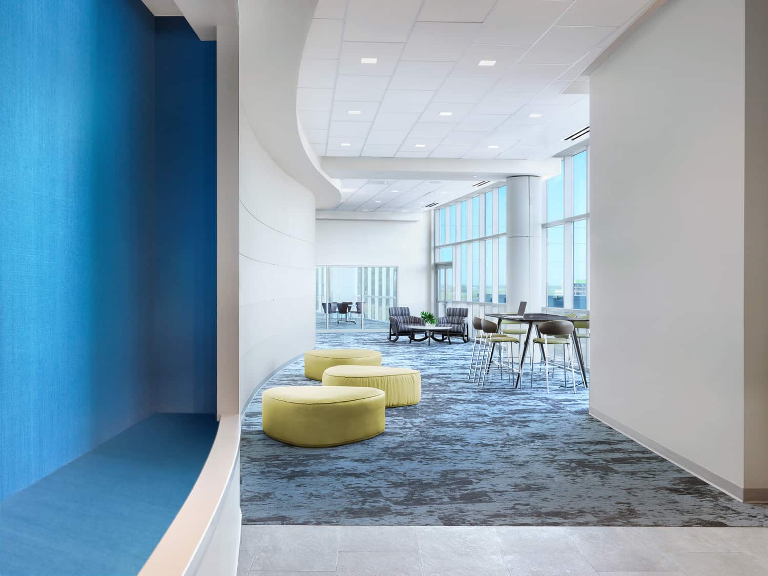 A modern corridor with curved walls to match the ceiling, which has different heights separated by curves. The spacious room has floor-to-ceiling windows on the right side and modern green furniture. This photo showcases BSA's expertise in interior design.
