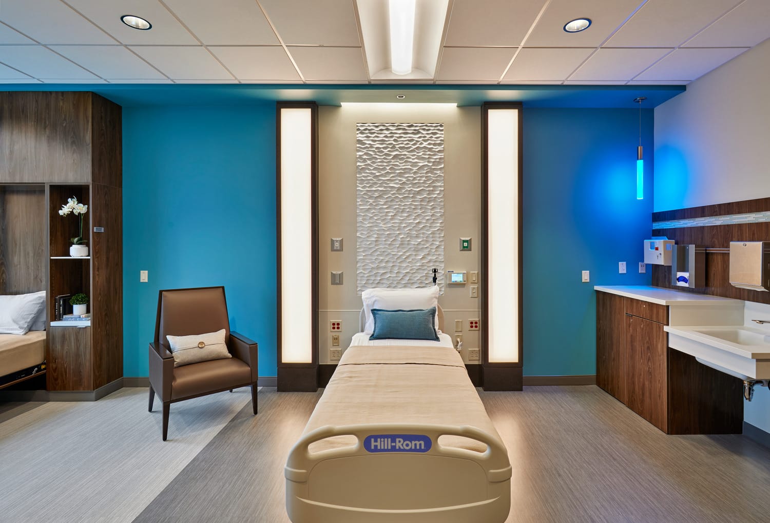 This image shows a close up of a patient bed within the Indiana Spine Hospital with a modern, organic art piece behind the bed. The room has a luxury feel, despite being the standard room. Warm wooden accents contribute to the luxury feel.This image shows BSA's expertise in interior design, specifically our expertise in designing attractive spaces that enhance patient care.