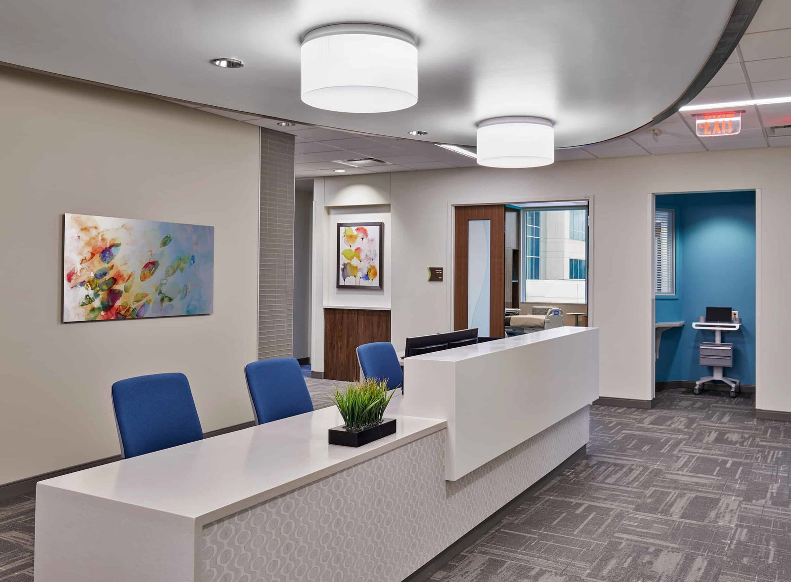 A provider work area with a large, white marble desk and three blue office chairs sit in the middle of the Indiana Spine Hospital. Doors are open in the background and offer a sneak peak into modern inpatient rooms with blue walls.