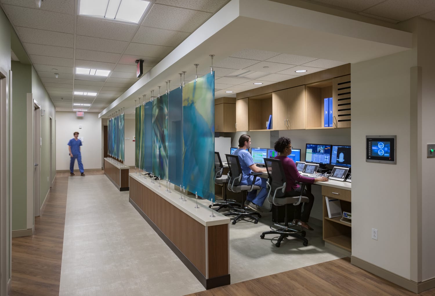 The Phelps Health Delbert Day Cancer Institute's provider work area, which is separated from a hallway with blue and green glass panels. Doctors are sitting at community desks and looking at patient MRI imaging. This image showcases BSA's expertise in designing spaces that are functional for healthcare professionals.