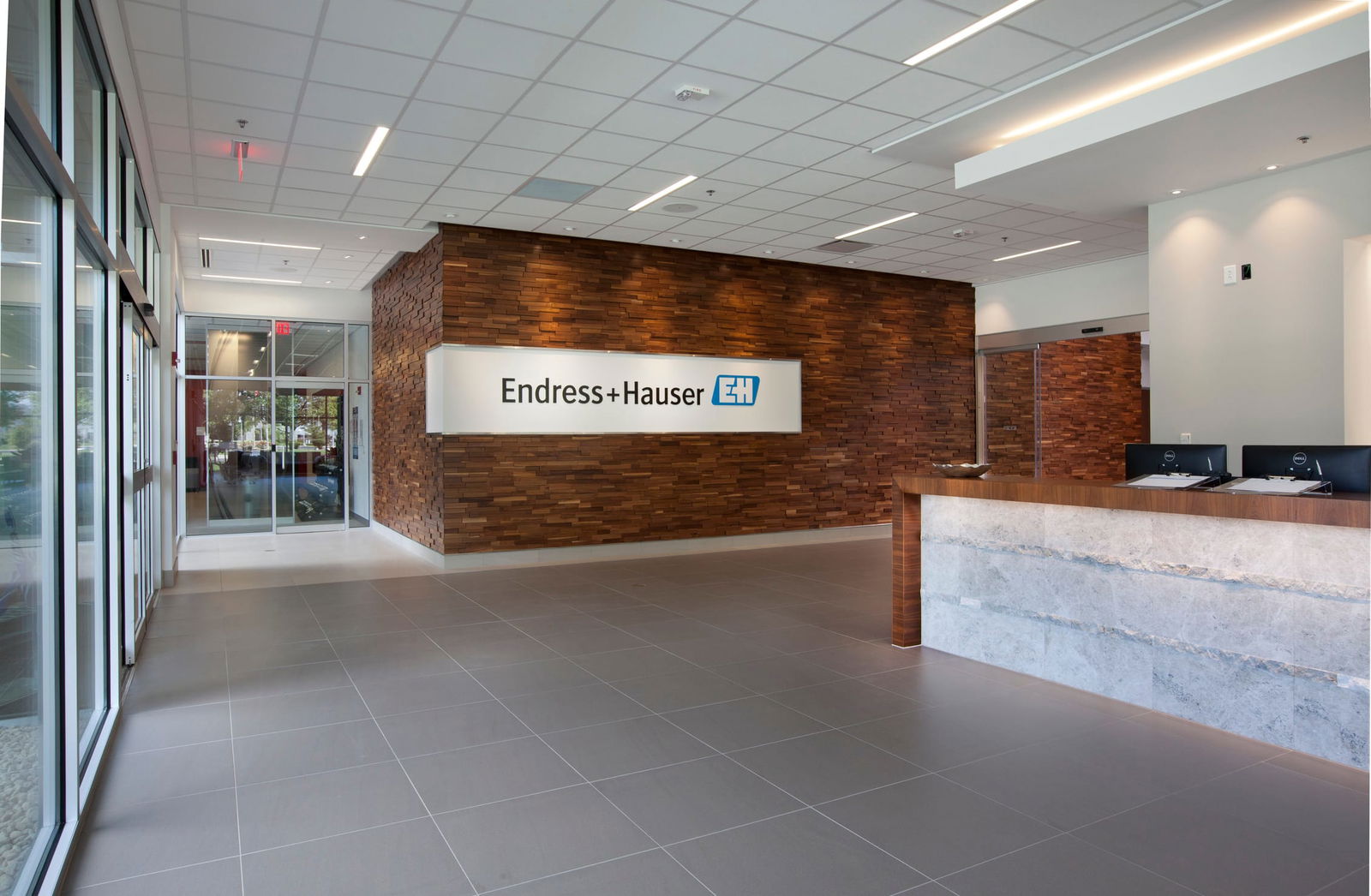 Reception area of the Endress+Hauser Customer Center featuring a modern stone and wood reception desk. To the left is a warm wood accent wall prominently featuring the Endress+Hauser logo, showing strong brand identity.