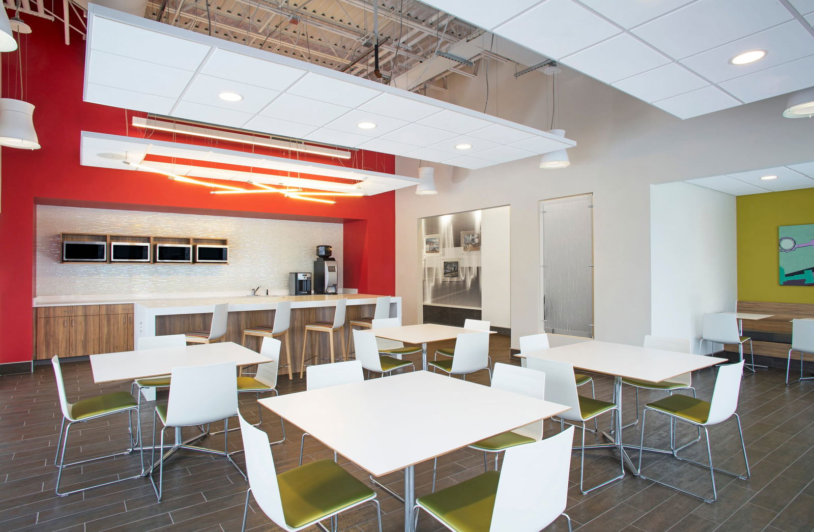 A vibrant break space within the Wetzer Production Center invites creativity and collaboration beyond the lab. The bold red accent wall energizes the room, while the clean-lined furniture and white acoustic ceiling panels maintain a modern, minimal feel. A tiled backsplash and integrated microwaves provide practical convenience, and the warm wood tones of the cabinetry and stools bring a sense of comfort. Pops of green on chair seats echo the center’s connection to innovation and sustainability. Whether it’s a quick coffee break or an informal brainstorming session, this space supports the people who bring ideas to life.