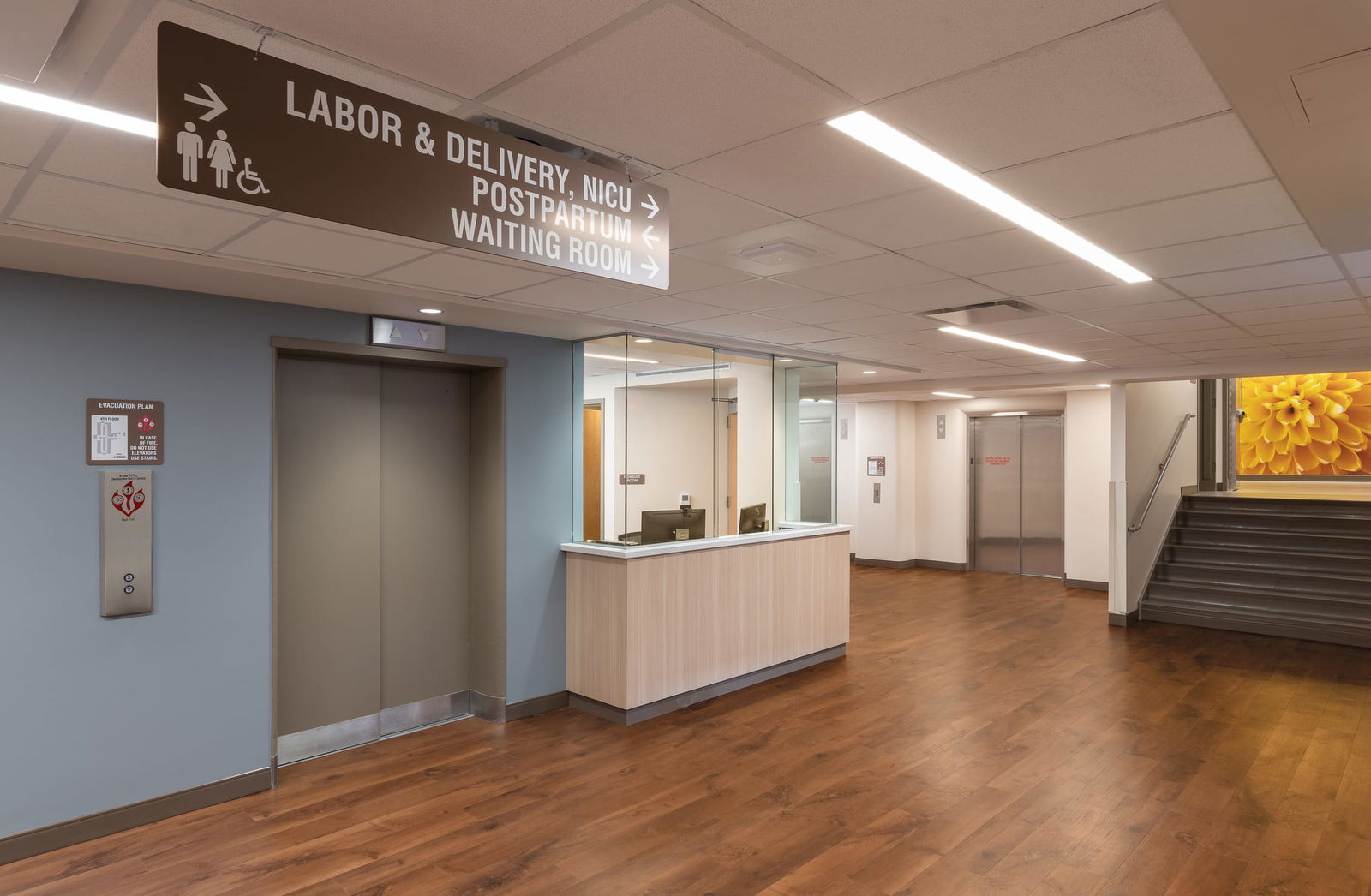 This image shows a reception or check-in area of the Cheyenne Regional Medical Center's maternal care department. A prominent brown directional sign hangs from the ceiling with symbols for men, women, and accessibility, indicating
